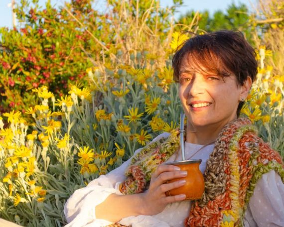 A woman smiles while drinking traditional mate among yellow flowers in Montevideo.